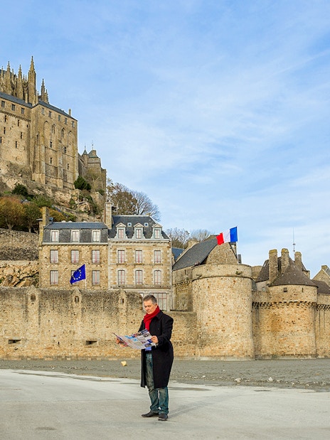 Visitor reading map in front of Mont-Saint-Michel Abbey, France.