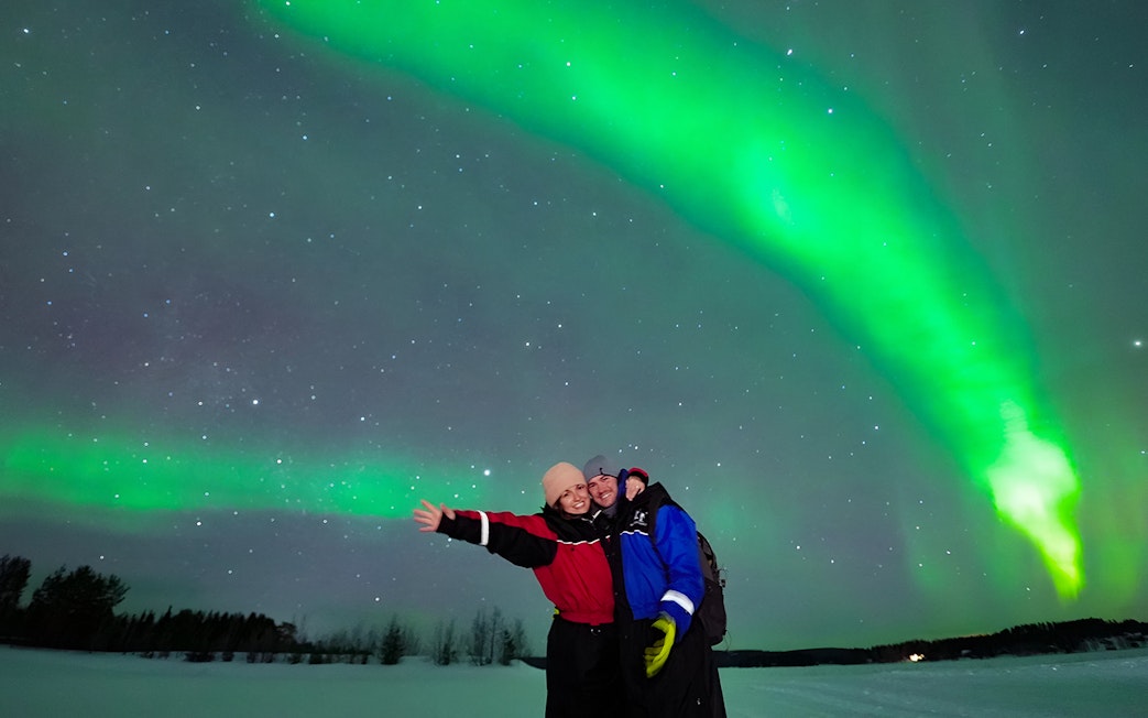 Tourists enjoying the Northern Lights display in a snowy landscape.