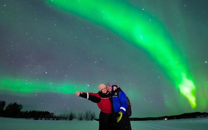 Tourists enjoying the Northern Lights display in a snowy landscape.