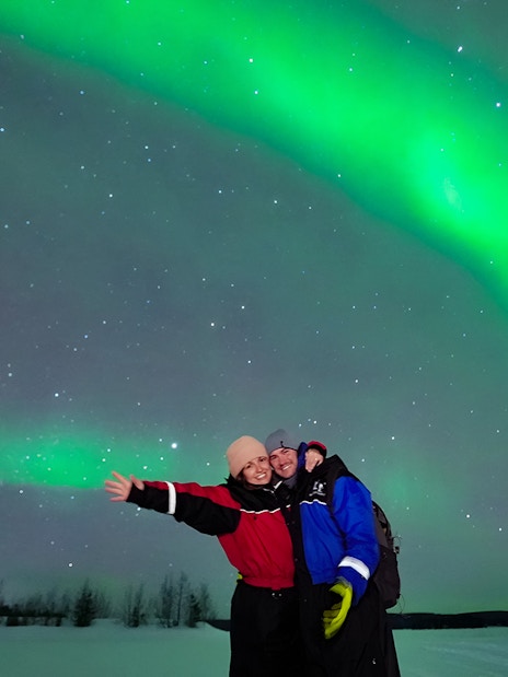 Tourists enjoying the Northern Lights display in a snowy landscape.