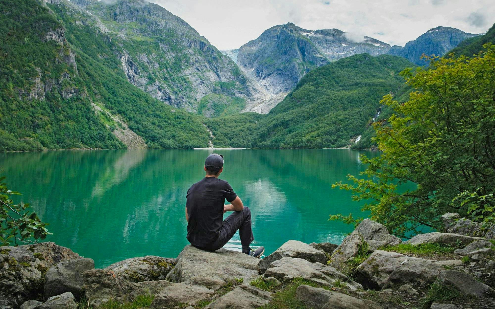 Person sitting by Bondhusvatnet Lake, surrounded by mountains, Folgefonna National Park, Norway.
