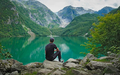 Person sitting by Bondhusvatnet Lake, surrounded by mountains, Folgefonna National Park, Norway.