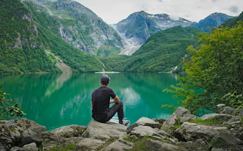 Person sitting by Bondhusvatnet Lake, surrounded by mountains, Folgefonna National Park, Norway.