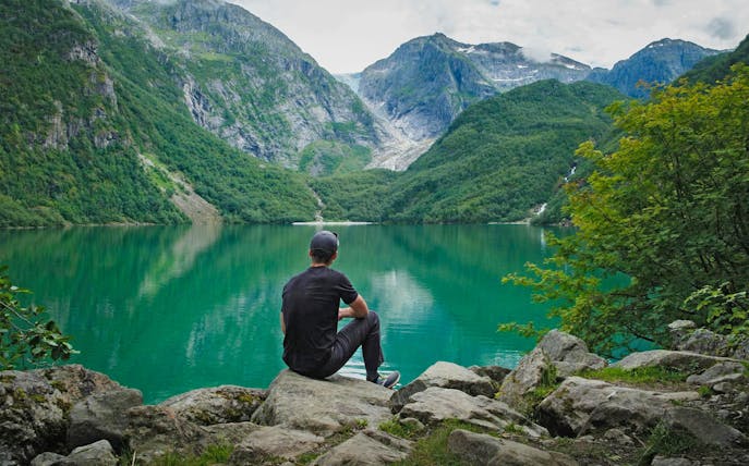 Person sitting by Bondhusvatnet Lake, surrounded by mountains, Folgefonna National Park, Norway.