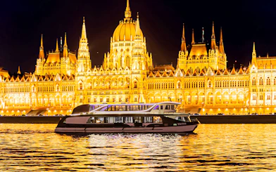 Cruise boat on the Danube River with Budapest Parliament illuminated at night.