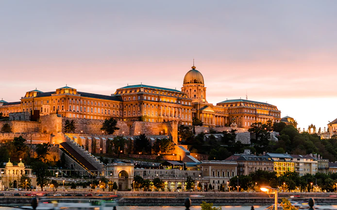 Buda Castle illuminated at night in Budapest, Hungary, with a sunset sky.