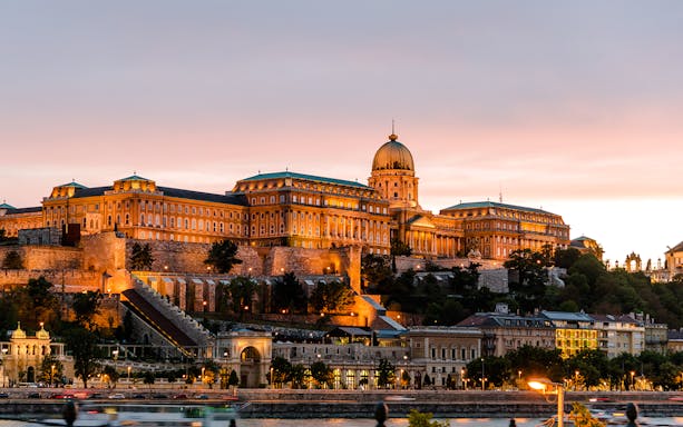 Buda Castle illuminated at night in Budapest, Hungary, with a sunset sky.