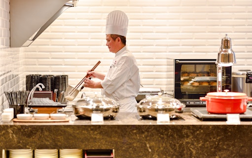 Chef preparing food in Plaza Premium Lounge kitchen, Singapore airport.