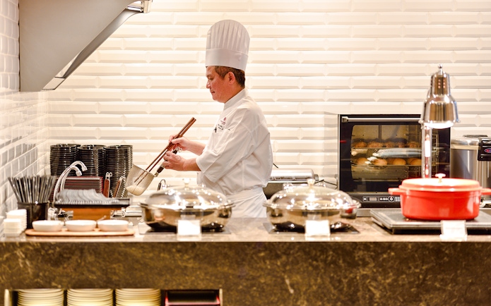 Chef preparing food in Plaza Premium Lounge kitchen, Singapore airport.
