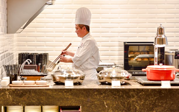 Chef preparing food in Plaza Premium Lounge kitchen, Singapore airport.