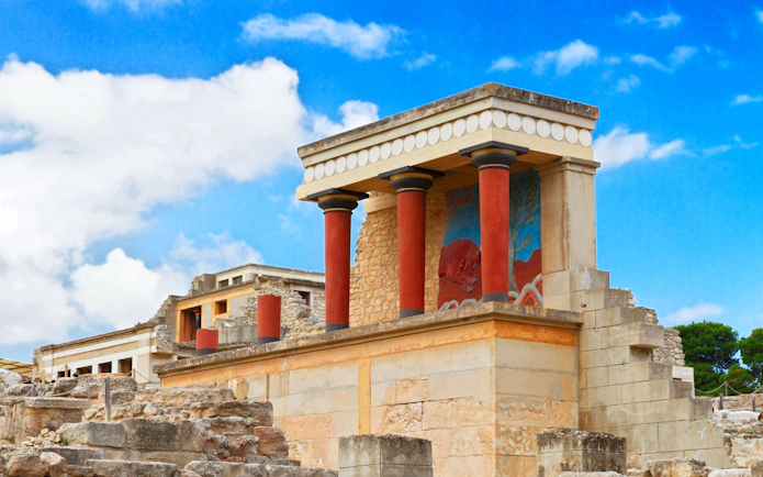 Knossos Palace ruins with red columns and fresco in Crete, Greece.
