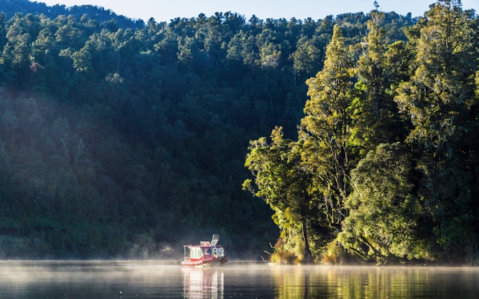 Boat cruising on Lake Mapourika surrounded by lush forest.