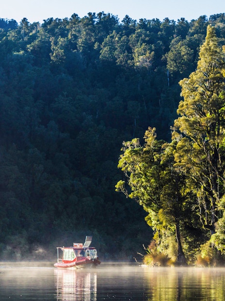 Boat cruising on Lake Mapourika surrounded by lush forest.