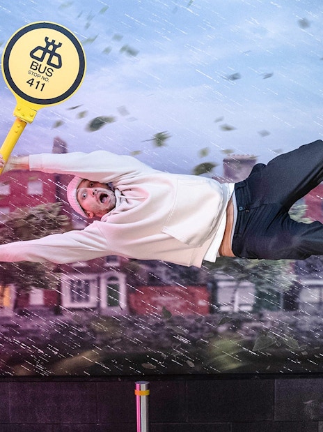 Guest clinging to a tilted bus stop sign at World of Illusions, creating a gravity-defying effect.