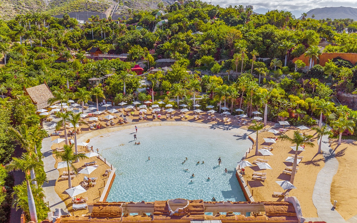 Tourists swimming and relaxing at Coco Beach, Siam Park, surrounded by lush greenery.