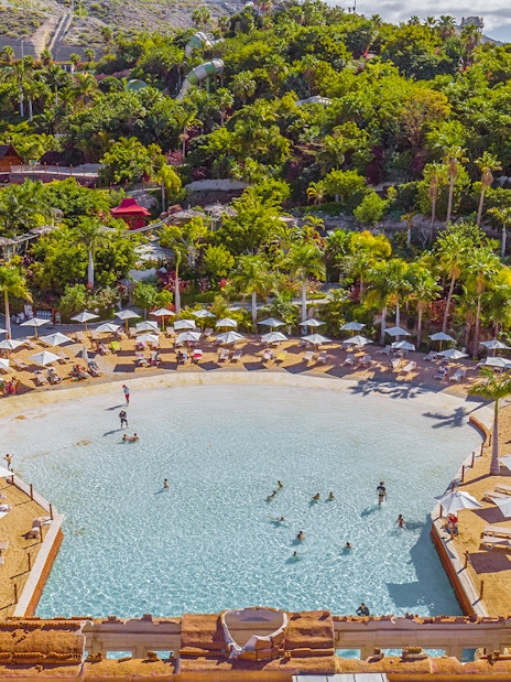 Tourists swimming and relaxing at Coco Beach, Siam Park, surrounded by lush greenery.