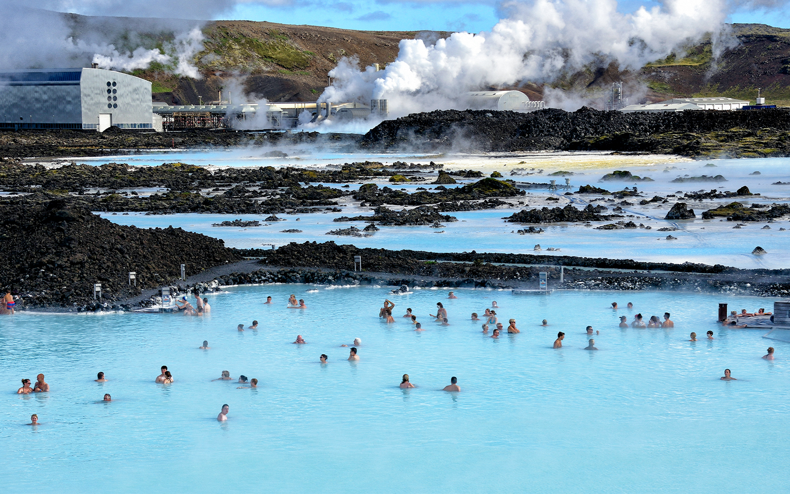 Bathers in Blue Lagoon hot springs with Svartsengi Geo-Thermal Plant in the background, Iceland.