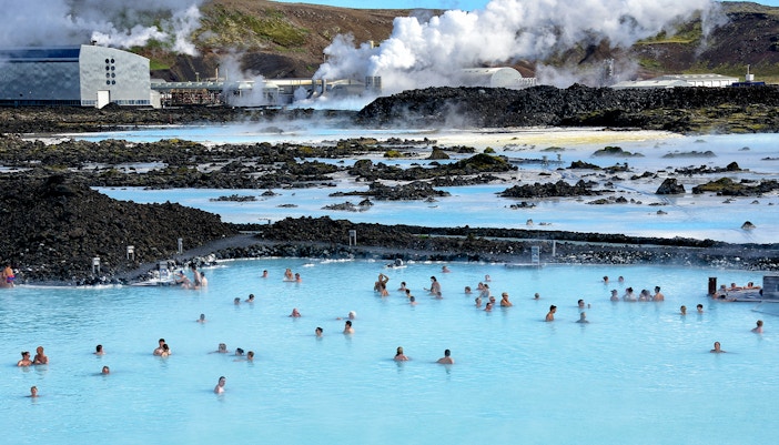 Bathers in Blue Lagoon hot springs with Svartsengi Geo-Thermal Plant in the background, Iceland.