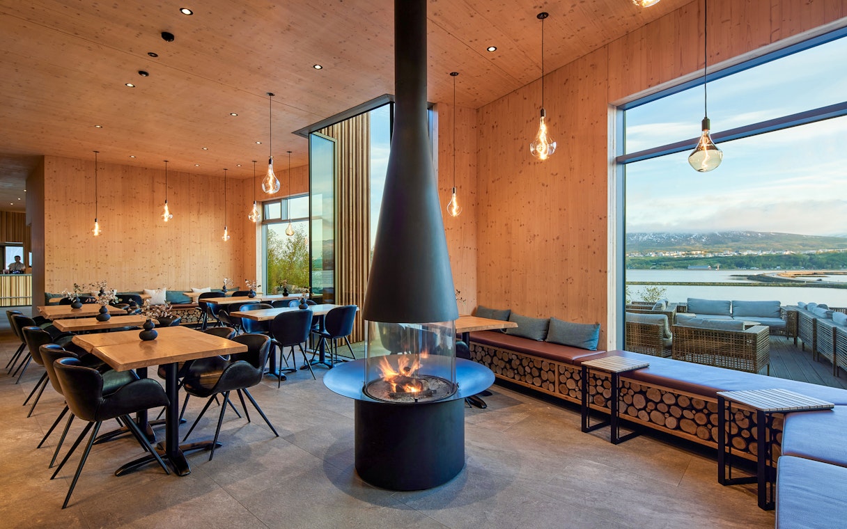 Bistro interior at Forest Lagoon spa with fireplace and view of Vaðlaskógur forest near Akureyri, North Iceland.