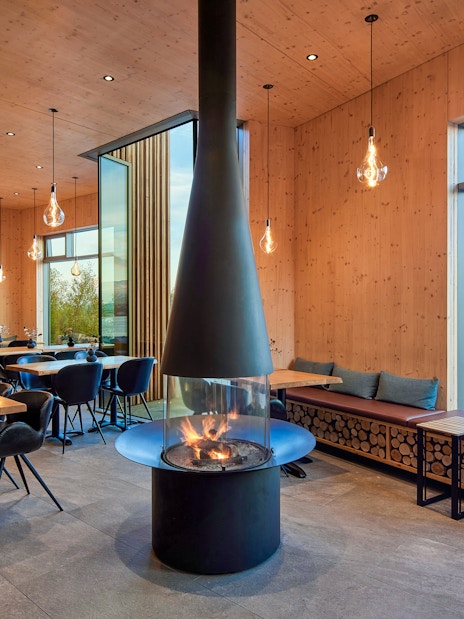 Bistro interior at Forest Lagoon spa with fireplace and view of Vaðlaskógur forest near Akureyri, North Iceland.