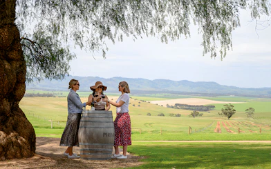 Three people enjoying wine at a barrel table with Barossa Valley vineyards in the background.