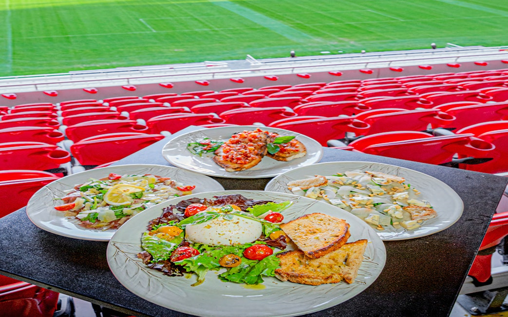Plates of food at a restaurant overlooking Benfica Stadium's field.