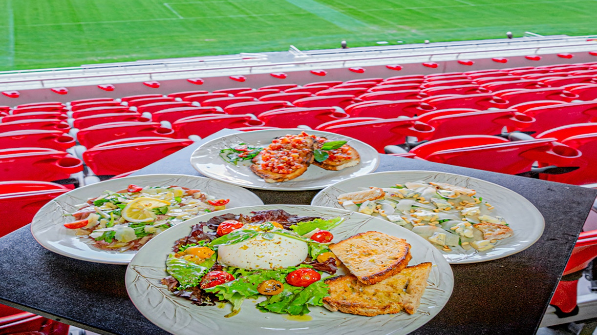 Plates of food at a restaurant overlooking Benfica Stadium's field.