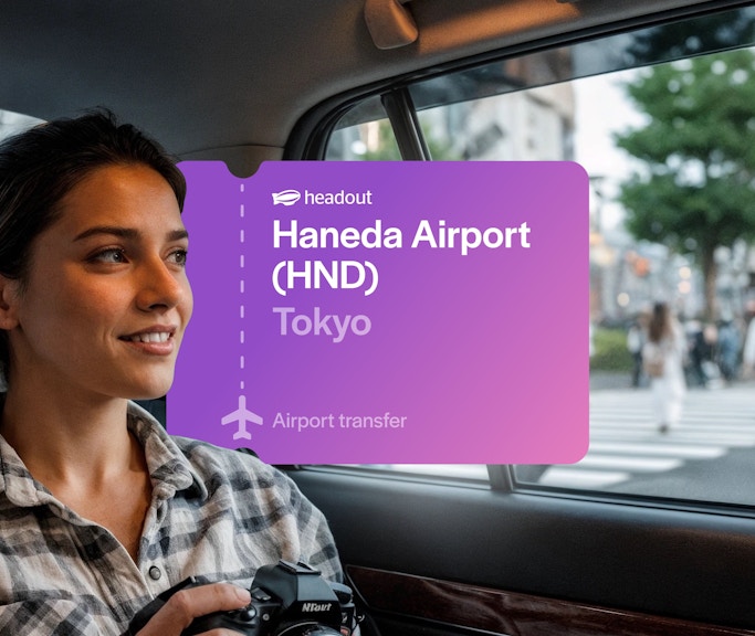 Woman holding camera in car passing through Shibuya, Tokyo with Haneda Airport transfer sign.