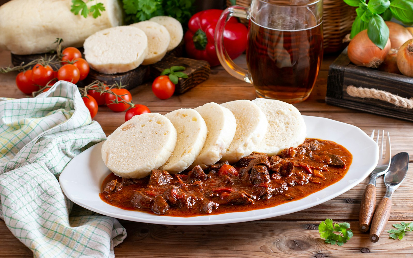 Czech goulash with dumplings on a plate, surrounded by fresh tomatoes and herbs.