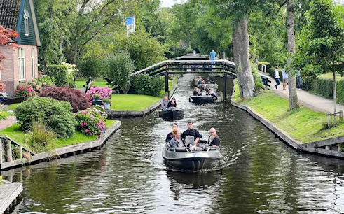 Boats navigating a canal in Giethoorn, surrounded by lush greenery and traditional Dutch houses.