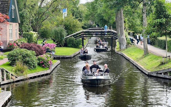 Boats navigating a canal in Giethoorn, surrounded by lush greenery and traditional Dutch houses.