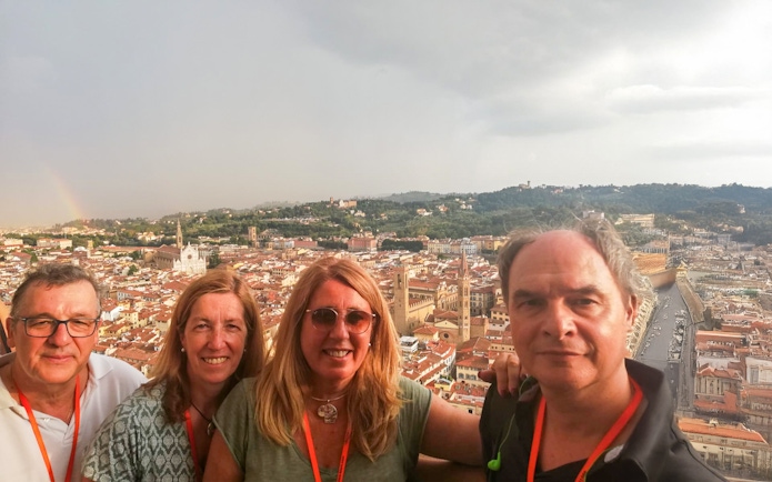 Group enjoying view from Brunelleschi’s Dome in Florence, Italy, with cityscape and rainbow in background.