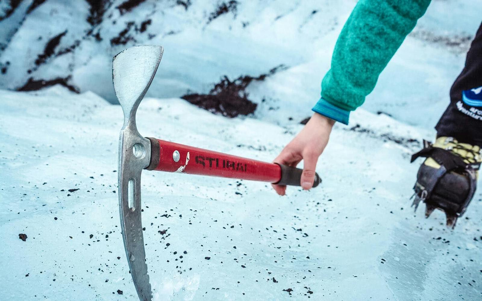 Hiker using ice axe on Sólheimajökull glacier tour in Iceland.
