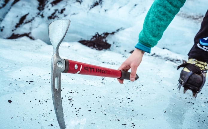 Hiker using ice axe on Sólheimajökull glacier tour in Iceland.