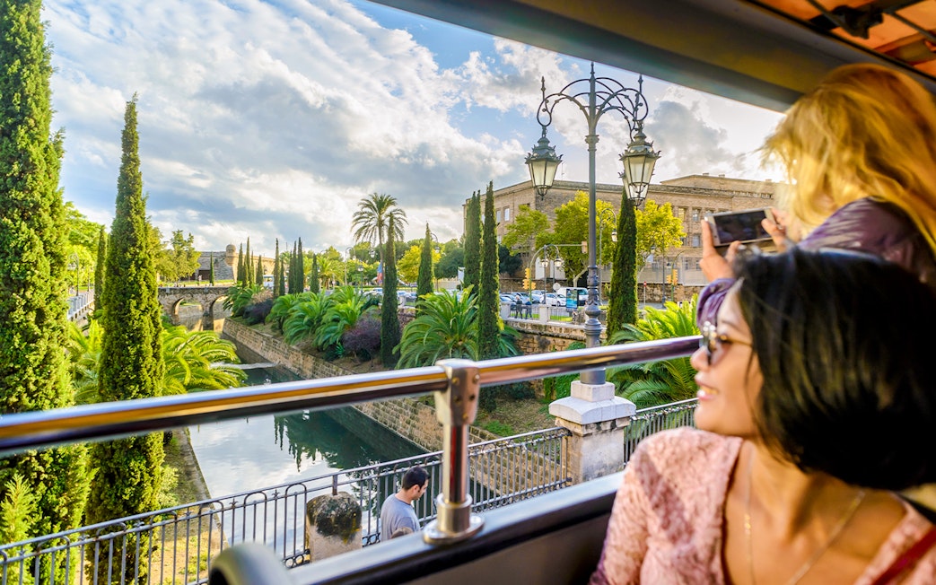 Tourists on Palma de Mallorca Hop-On Hop-Off Bus viewing city landmarks through large windows.