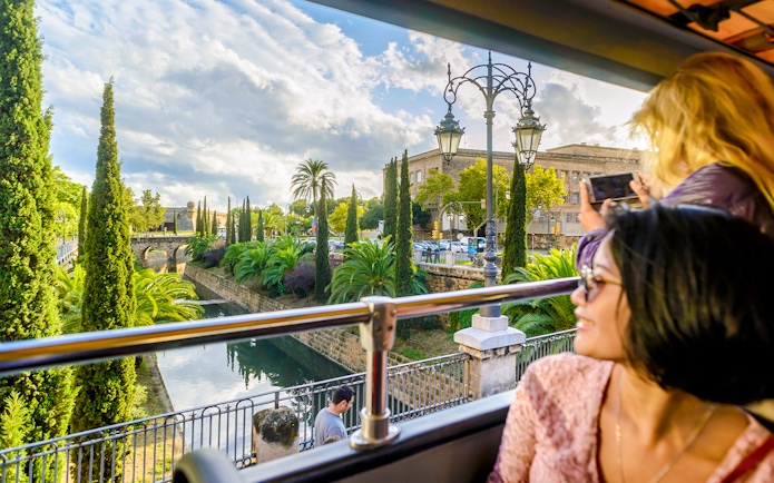 Tourists on Palma de Mallorca Hop-On Hop-Off Bus viewing city landmarks through large windows.