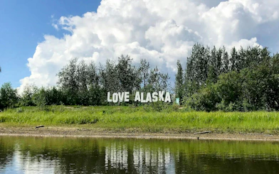 Love Alaska sign by a riverbank with trees in Fairbanks.