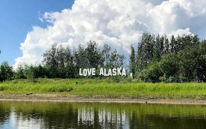 Love Alaska sign by a riverbank with trees in Fairbanks.