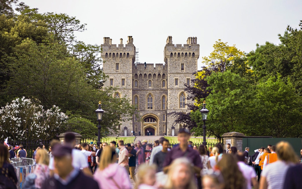 Crowd outside Windsor Castle entrance surrounded by trees.