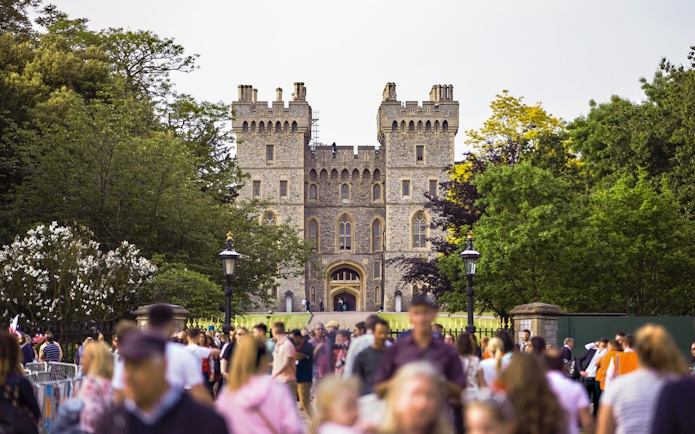 Crowd outside Windsor Castle entrance surrounded by trees.