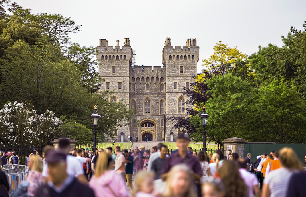 Crowd outside Windsor Castle entrance surrounded by trees.