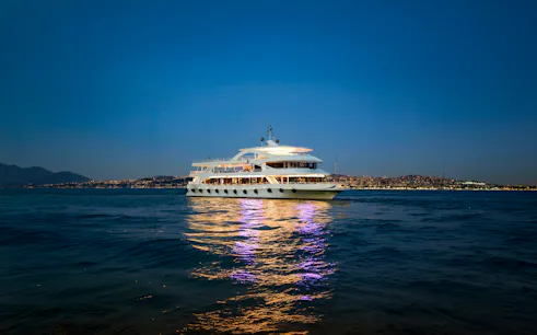 Multi-deck cruise ship sailing on the Bosphorus Strait in Istanbul, Turkey at dusk.