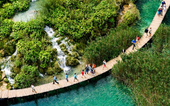 Visitors walking on a wooden path over turquoise water at Plitvice Lakes, Croatia.
