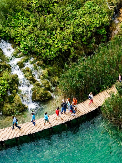 Visitors walking on a wooden path over turquoise water at Plitvice Lakes, Croatia.
