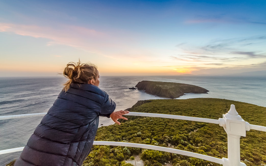 Woman enjoying sunset view from Bruny Island lighthouse balcony.