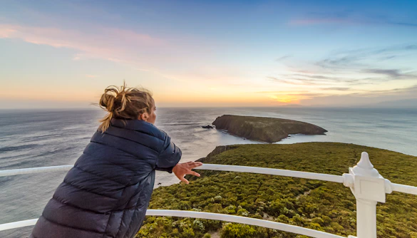 Woman enjoying sunset view from Bruny Island lighthouse balcony.