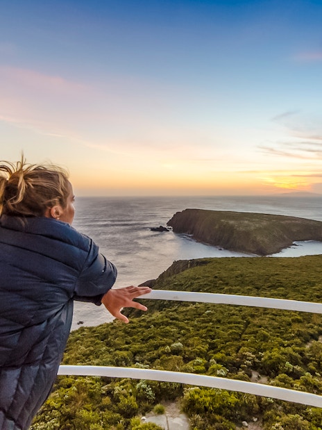 Woman enjoying sunset view from Bruny Island lighthouse balcony.
