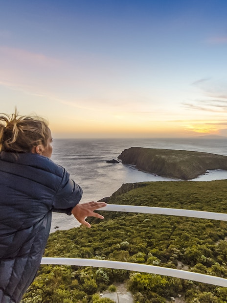 Woman enjoying sunset view from Bruny Island lighthouse balcony.