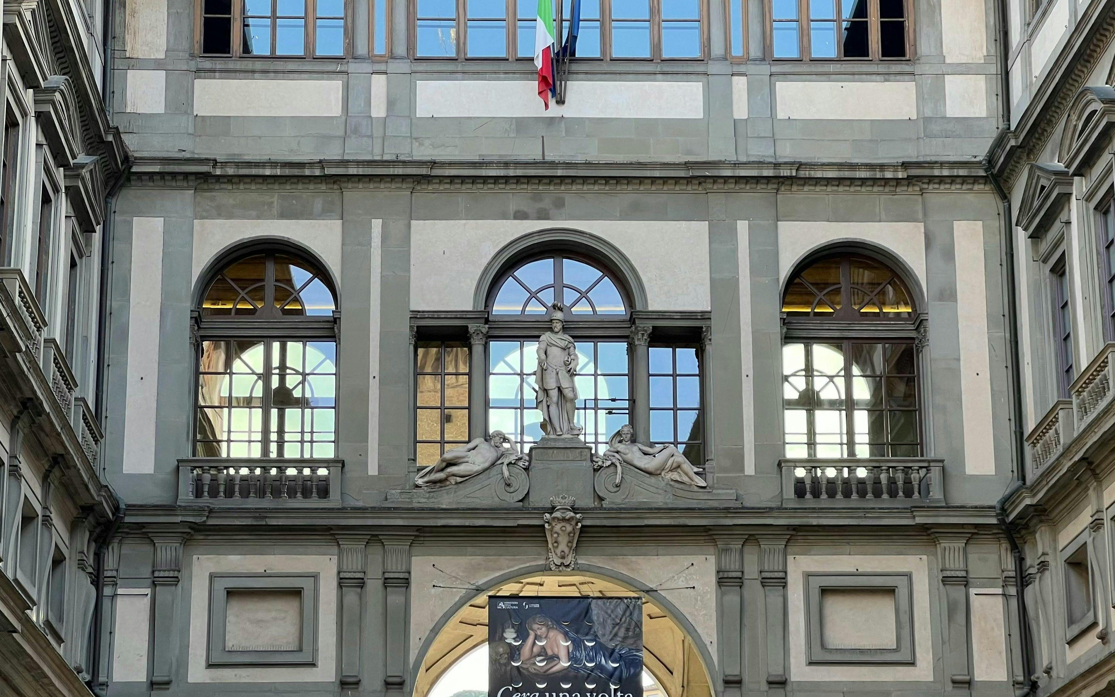 Facade of Uffizi Gallery in Florence with statues and Italian flag.