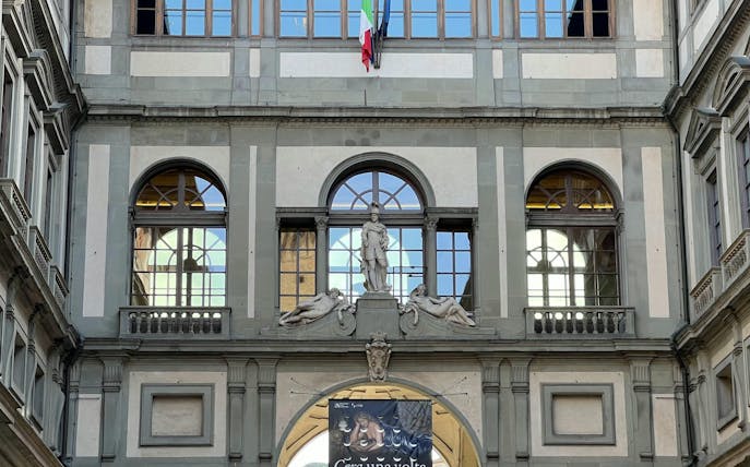 Facade of Uffizi Gallery in Florence with statues and Italian flag.